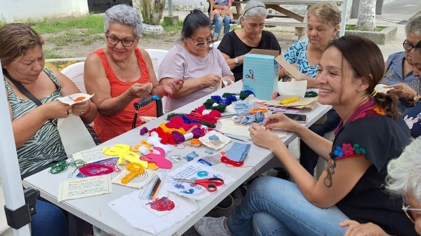 Group of women seated at a table crafting with yarn.