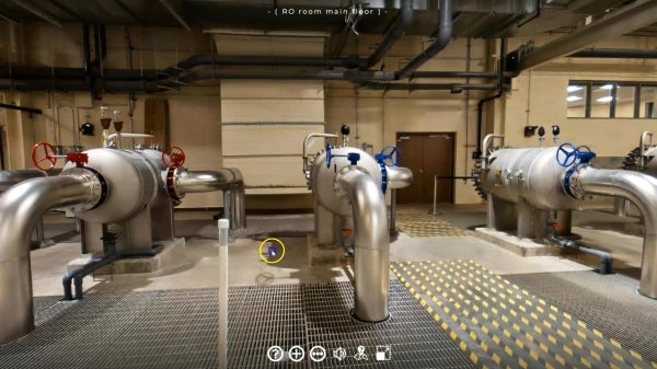 Industrial room in a water purification plant with large metal pumps, pipes and valves connected to machinery; gray gridded flooring with textured yellow patterns for traction highlights a workspace.