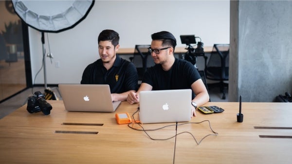 two students sitting at a desk working on laptops