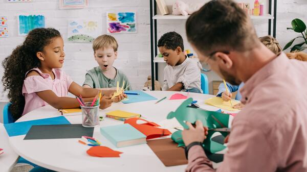 Preschoolers seated around a table with a teacher, playing with construction paper.