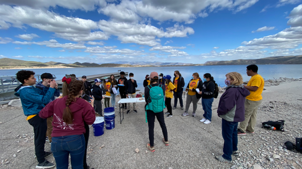 Group of students and teachers standing on the banks of a lake.