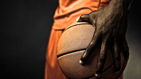 The hand of a Black basketball player gripping a basketball.