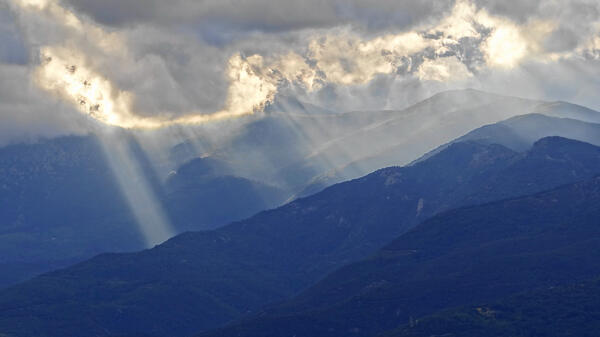 Light rays shining through clouds onto a mountainous landscape.