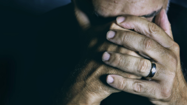 Stock image of an older man with his head in his hands. A wedding ring is visible