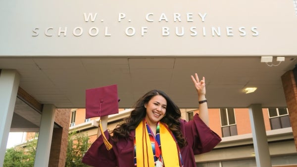 Berenice Pelayo in front of the WP Carey Business School in her cap and gown