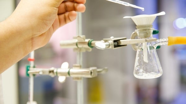 A hand using a dropper to drop liquid into a chemistry flask