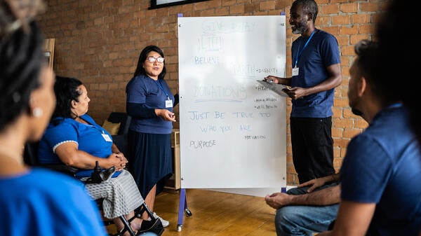 Two people up at white board talking with group from community