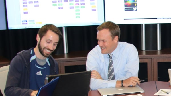 two men sitting at a table working on a computer