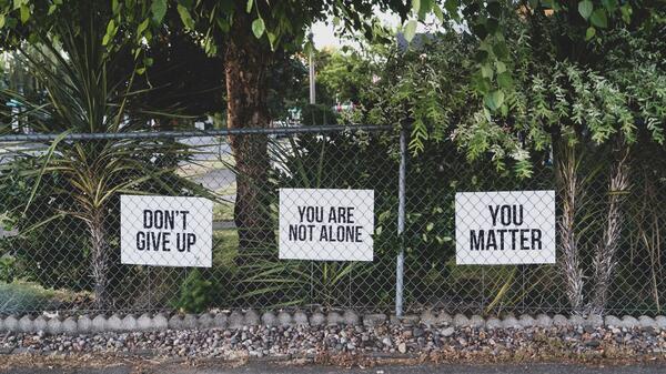 Three poster boards hung on a fence. They read "Don't give up," "You are not alone" and "You matter."