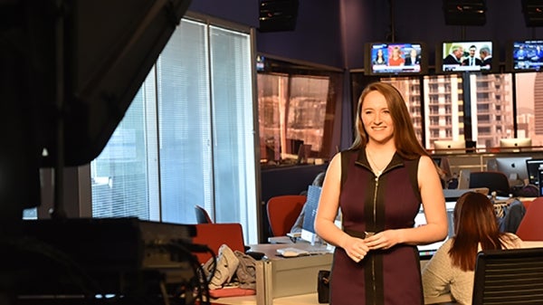 student in front of broadcast camera in newsroom