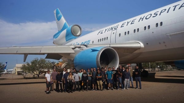 Group photo of ASU Professor of Practice Timothy Takahashi and members of the student groups AIAA@ASU and Air Devils standing next to a large plane.