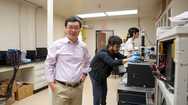 Hongbin Yu poses in front of his students conducting research in his lab in the background.