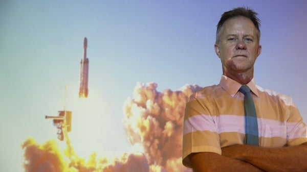 Hugh Barnaby stands in front of a projection of a SpaceX Falcon Heavy rocket launch. 