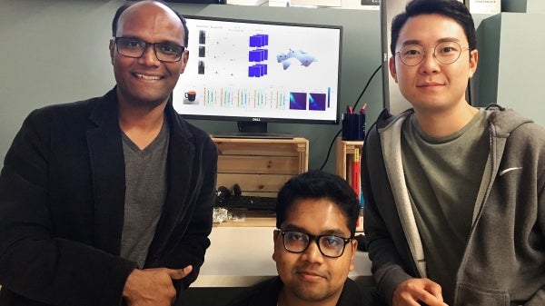 Three men posing in front of monitor