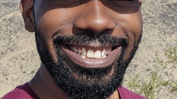 Close up image of PhD graduate Ed Buie II wearing a ball cap, smiles in front of a desert landscape.