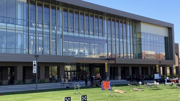 Various games such as giant Connect Four and cornhole are set up in the grass outside a gym complex.