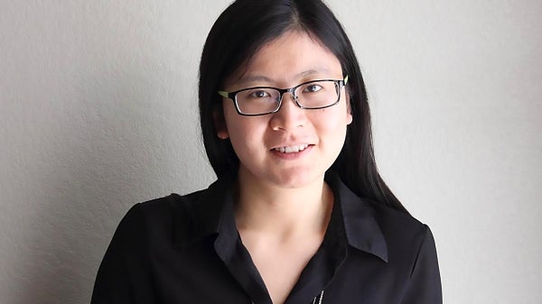 Fengxiu Zhang, a female with long dark hair and black-rimmed glasses faces the camera, smiling in a dark top