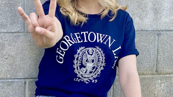 Victoria Stratton smiles wearing a Georgetown Law shirt and holding her fingers in a pitchfork symbol