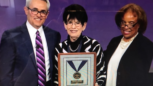 three people posing for photo, with woman in middle holding award