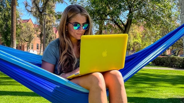 Student sitting in a hammock on ASU's Tempe campus working on a laptop.