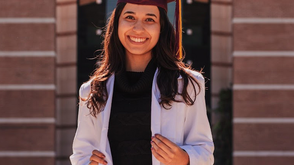 Hasti Asrari smiling and wearing a graduation cap in front of a building.