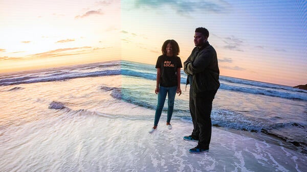 ASU Local students Kara Smith and Bryan Daniels stand in front of Planar Studio screens displaying a beach scene.