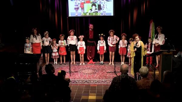 Children onstage singing with an older woman.