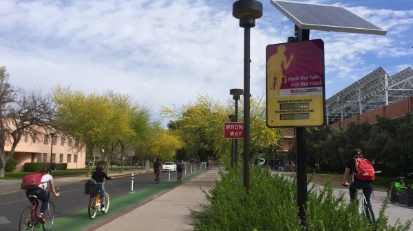 Bicyclists ride past the bike counter at College and Apache