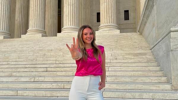 Logan Higgins on the steps of the Supreme Court doing the forks up hand gesture.