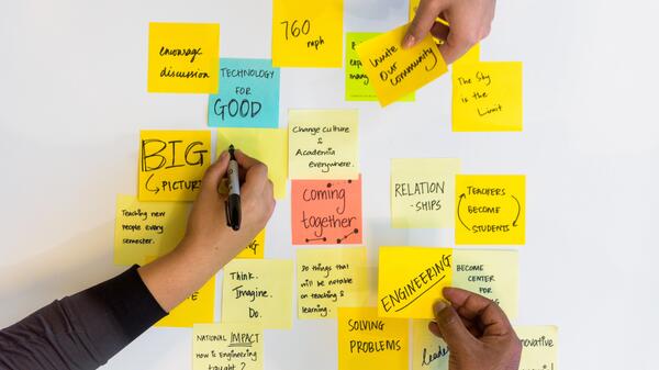 Three hands write ideas down and place sticky notes next to each other on a table 