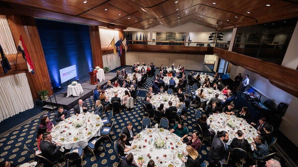 A room of people sitting at round banquet tables.