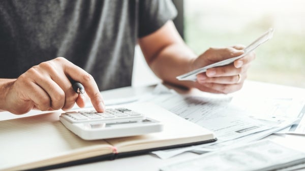 Hand typing on a calculator on a table full of papers.