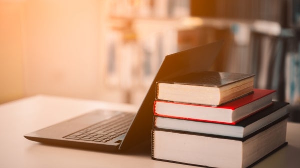 A laptop next to a stack of books