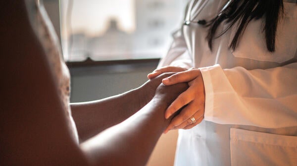 A doctor holds a patient's hands, with neither face visible