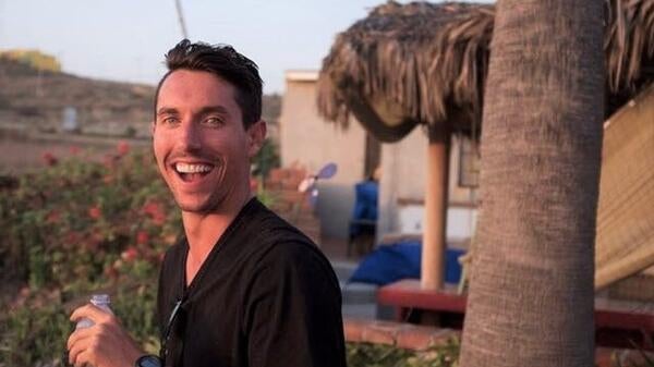 James Bennett stands near a palm tree in a village setting.