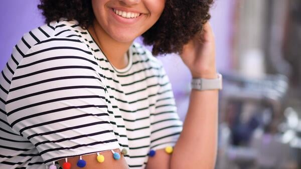 Photo of Jayla Johnson smiling and wearing a striped dress against a partly purple background