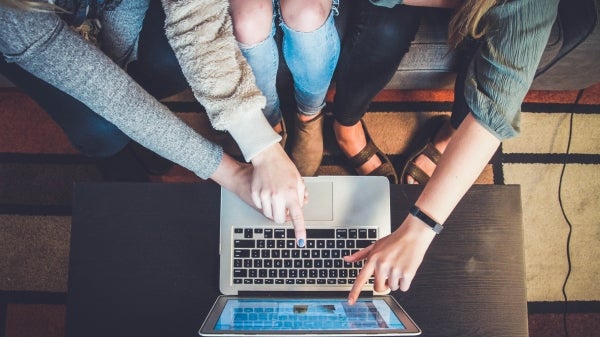 overhead shot of people sitting on a couch and pointing at a laptop screen