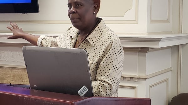 Beatrice A. Bunyasi of Kenyatta University speaks during a symposium at ASU in April. She has orange hair and is wearing a button-up shirt. She stands at a podium with a laptop sitting on it.