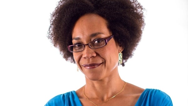 A photo of PhD student Kenja Hassan against a white backdrop. She's wearing glasses and a blue blouse.