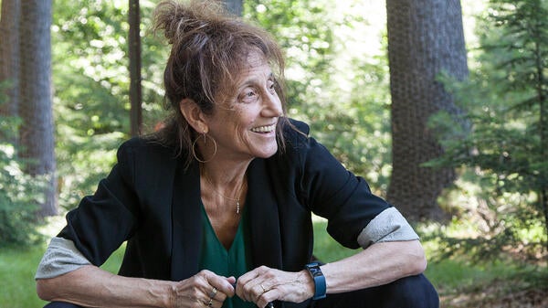 Liz Lerman sitting and looking to the side in a forest-like setting.