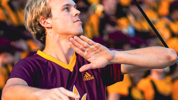 ASU graduating student twirling baton for ASU. Foreground is Cody with baton in action, background is blurred shot of audience in stadium