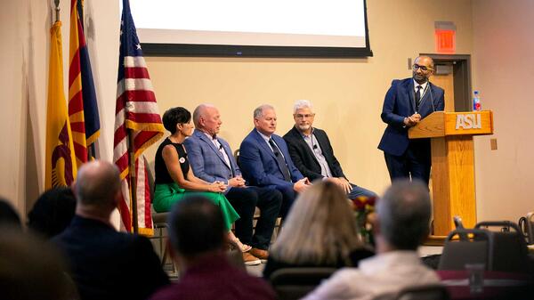 Group of speakers and panelists seated at MSN open house, on stage near a podium