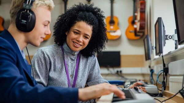 Student wearing headphones playing a keyboard as an instructor watches.