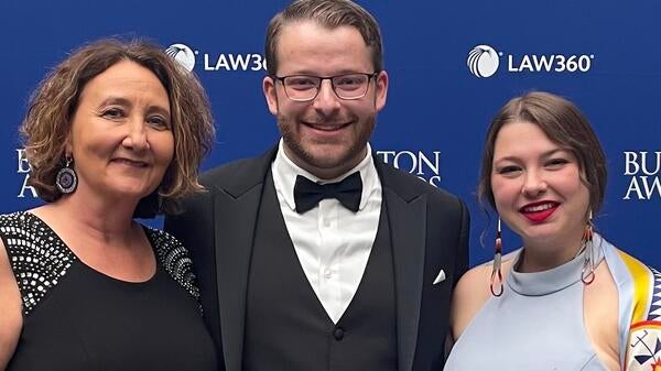 Two women and a man pose for a photo in front of a backdrop. 