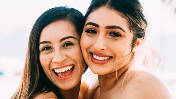 Two dark-haired women smiling and looking at the camera.