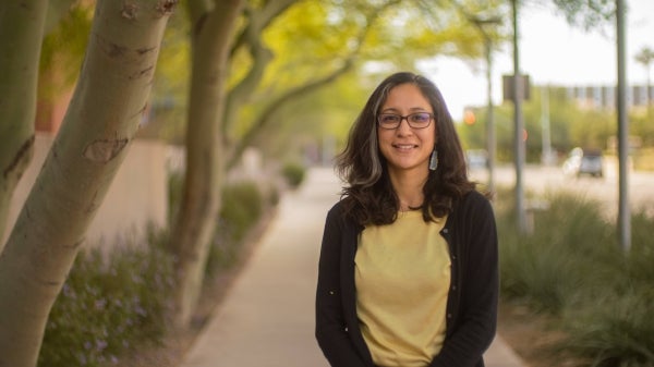 ASU Assistant Professor Viridiana Benitez smiling, looking at the camera, on a sidewalk lined with trees and bushes.