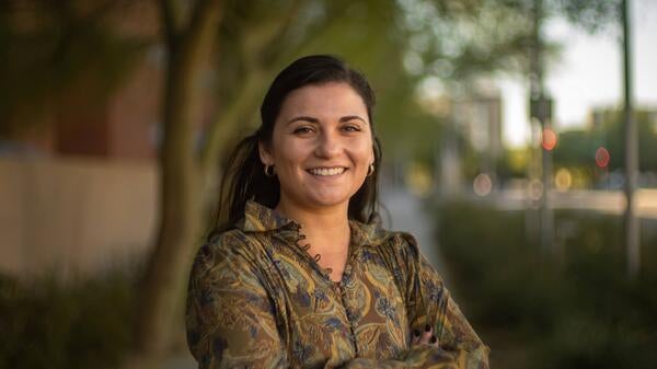 Holly Molinaro smiling, outside with a city street and trees in the background.