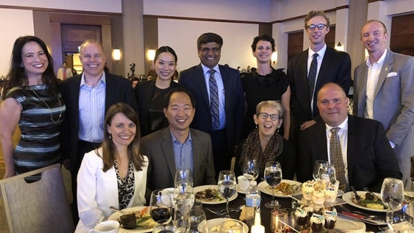 A group of people pose for a photo in a ballroom. Caption reads: Sethuraman Panchanathan poses for a photo with other ASU representatives at the Institute for Automated Mobility event. Photo by Vincent Orleck