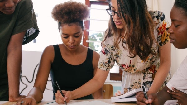 A group of students participating in active learning, surrounding a table and looking at and writing on a piece of paper.