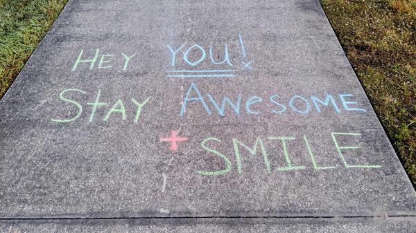 Sidewalk with chalk lettering that reads "Hey you! Stay awesome + smile."